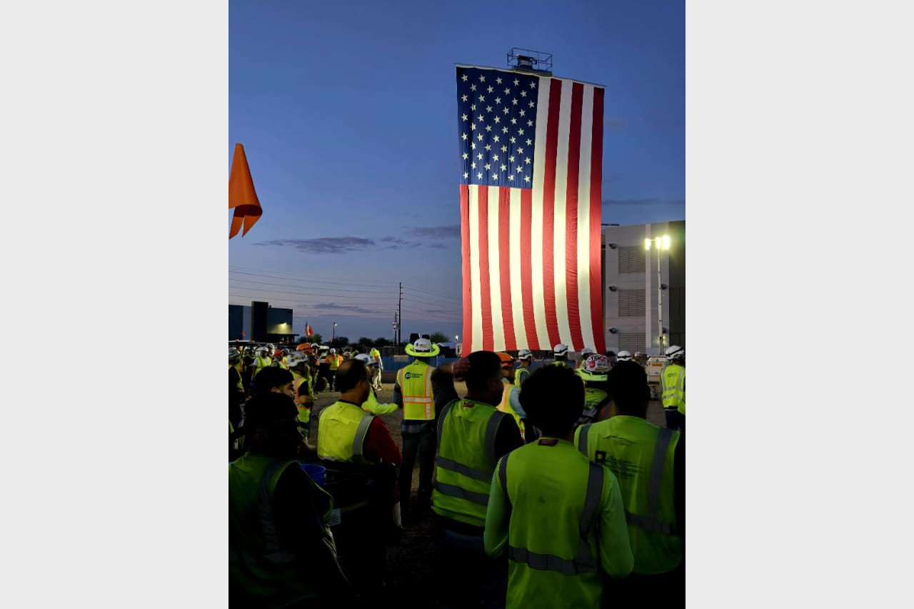 Workers watch a large American flag at dusk.