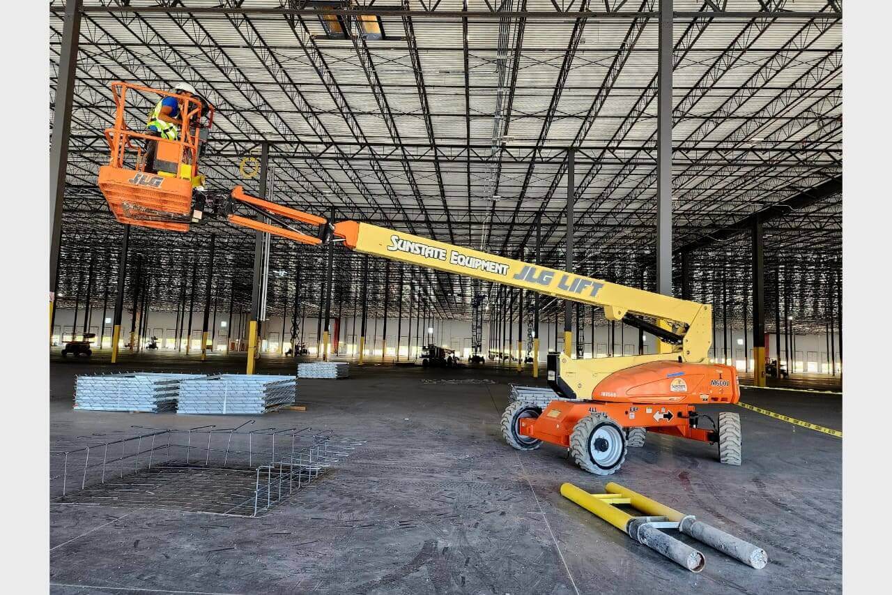 Construction workers operate a boom lift inside a large industrial building.