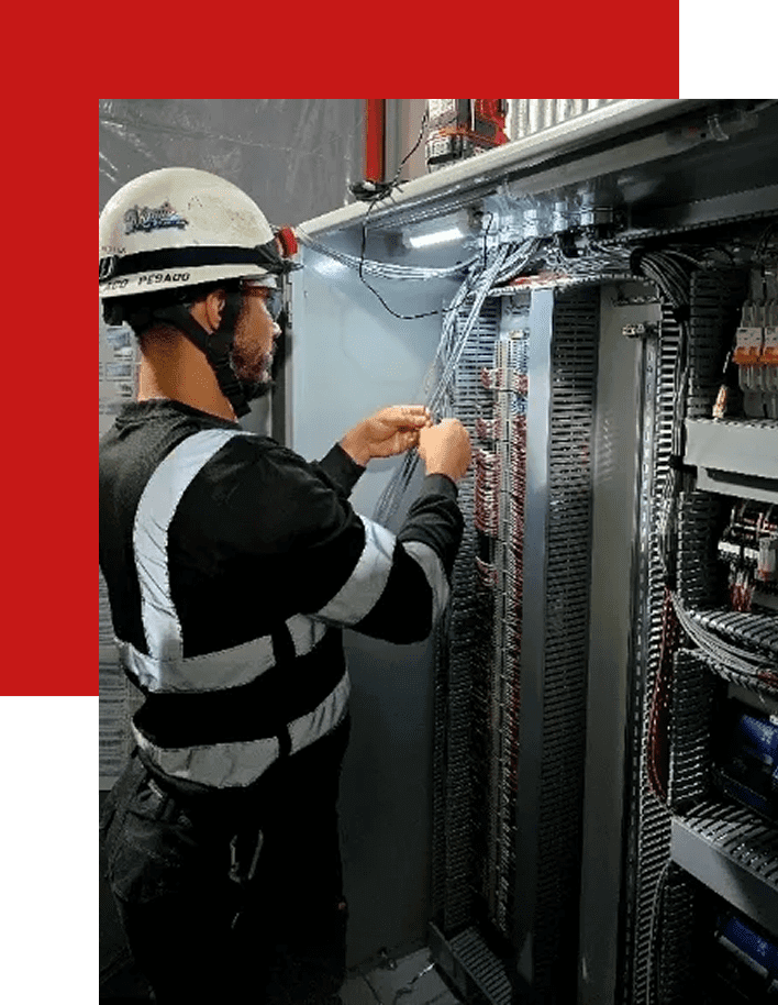 Electrician working on a control panel wiring in an industrial setting.